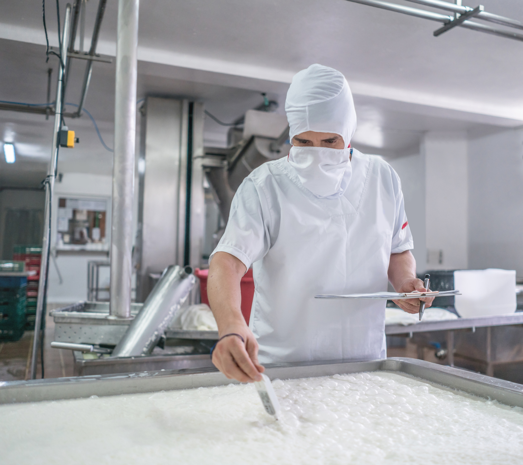 Eine Person mit Schutzkleid überprüft die Herstellung eines Milchproduktes. 
